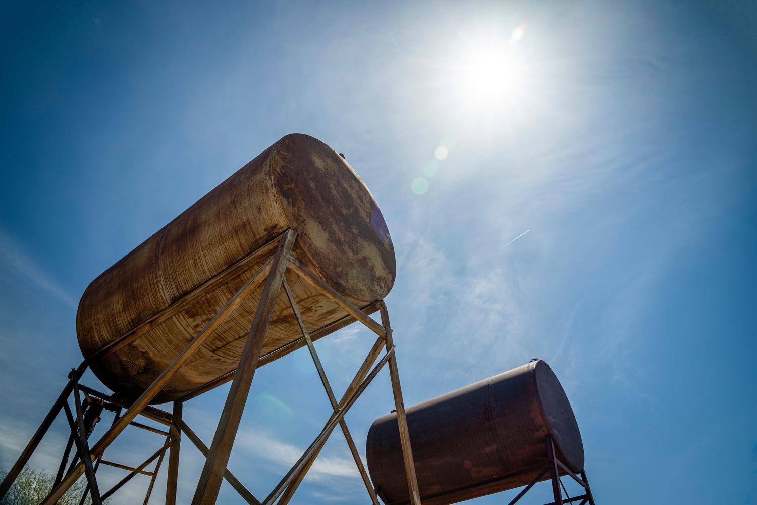 Tanques industriales de gasóleo oxidados bajo un cielo azul, representando el combustible fósil tradicional.