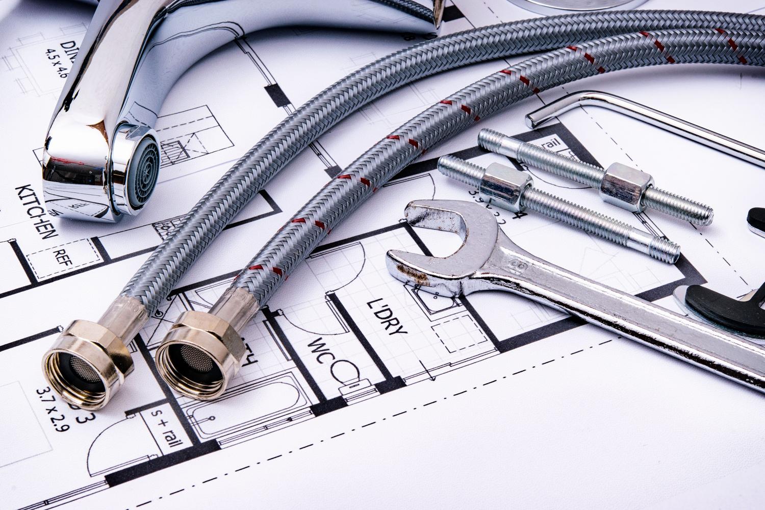 Herramientas de fontanería y grifería sobre un plano arquitectónico, representando la fase de planificación y diseño de instalaciones.