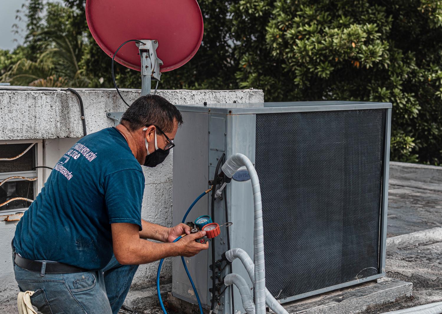 Técnico profesional realizando el mantenimiento preventivo de una unidad exterior de aire acondicionado utilizando manómetros de precisión. Técnico profesional realizando el mantenimiento preventivo de una unidad exterior de aire acondicionado utilizando manómetros de precisión.