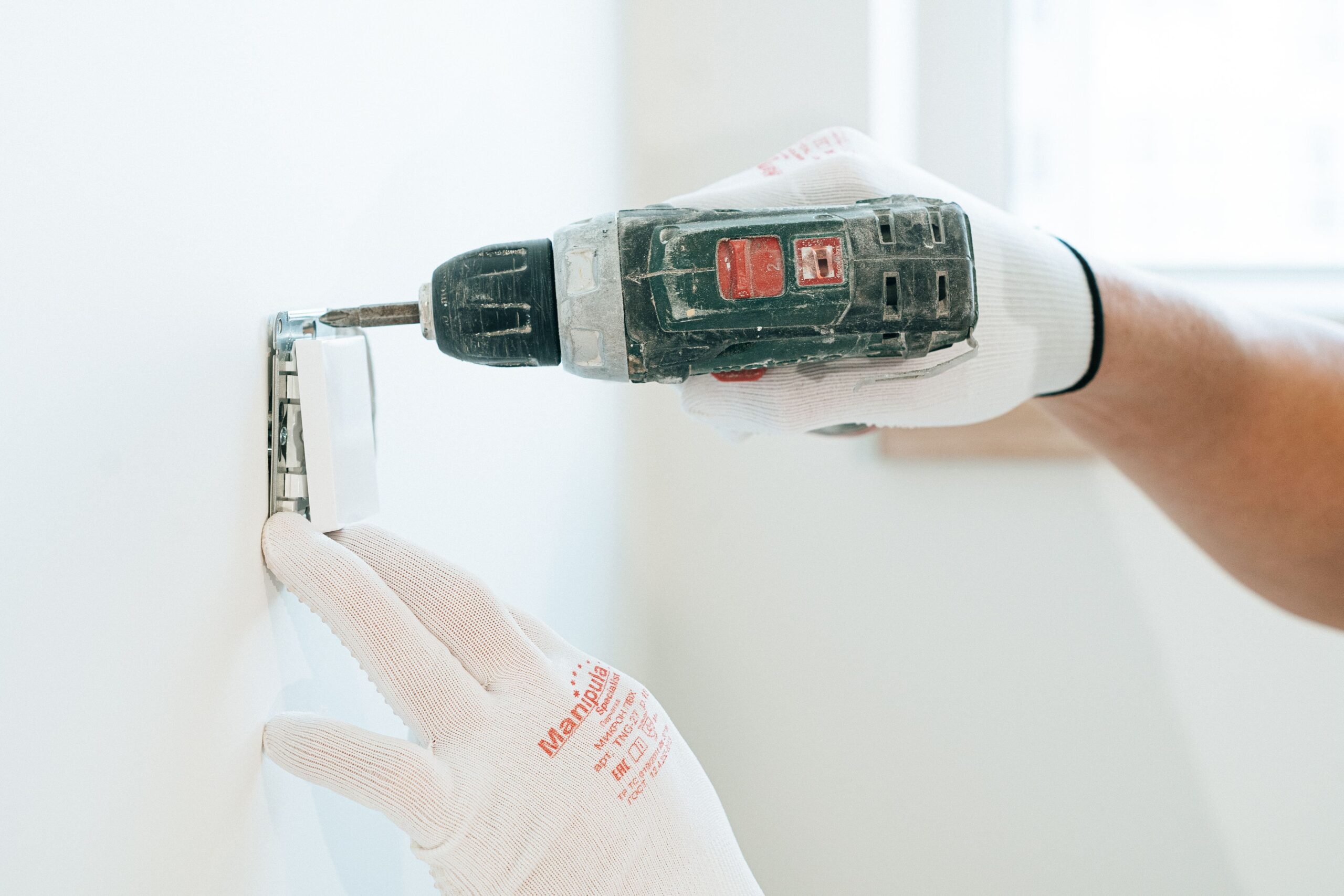 Instalación de un mecanismo eléctrico en la pared utilizando herramientas profesionales y guantes de seguridad para garantizar la precisión.