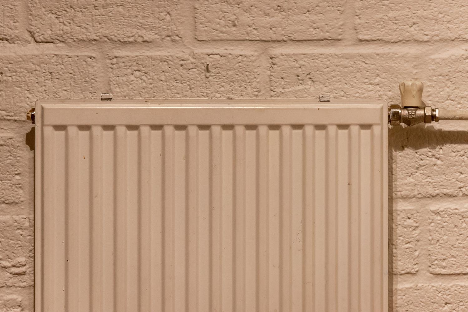 Radiador de aluminio blanco moderno instalado en una pared de ladrillo visto, ejemplo de emisor de calor eficiente.