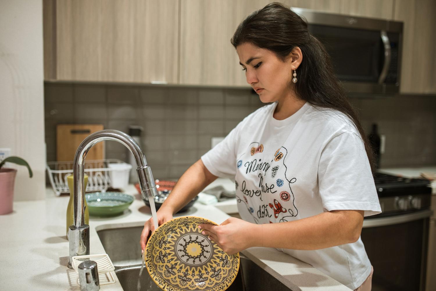 Persona lavando platos a mano en el fregadero, representando el método menos eficiente en consumo de agua comparado con el lavavajillas.