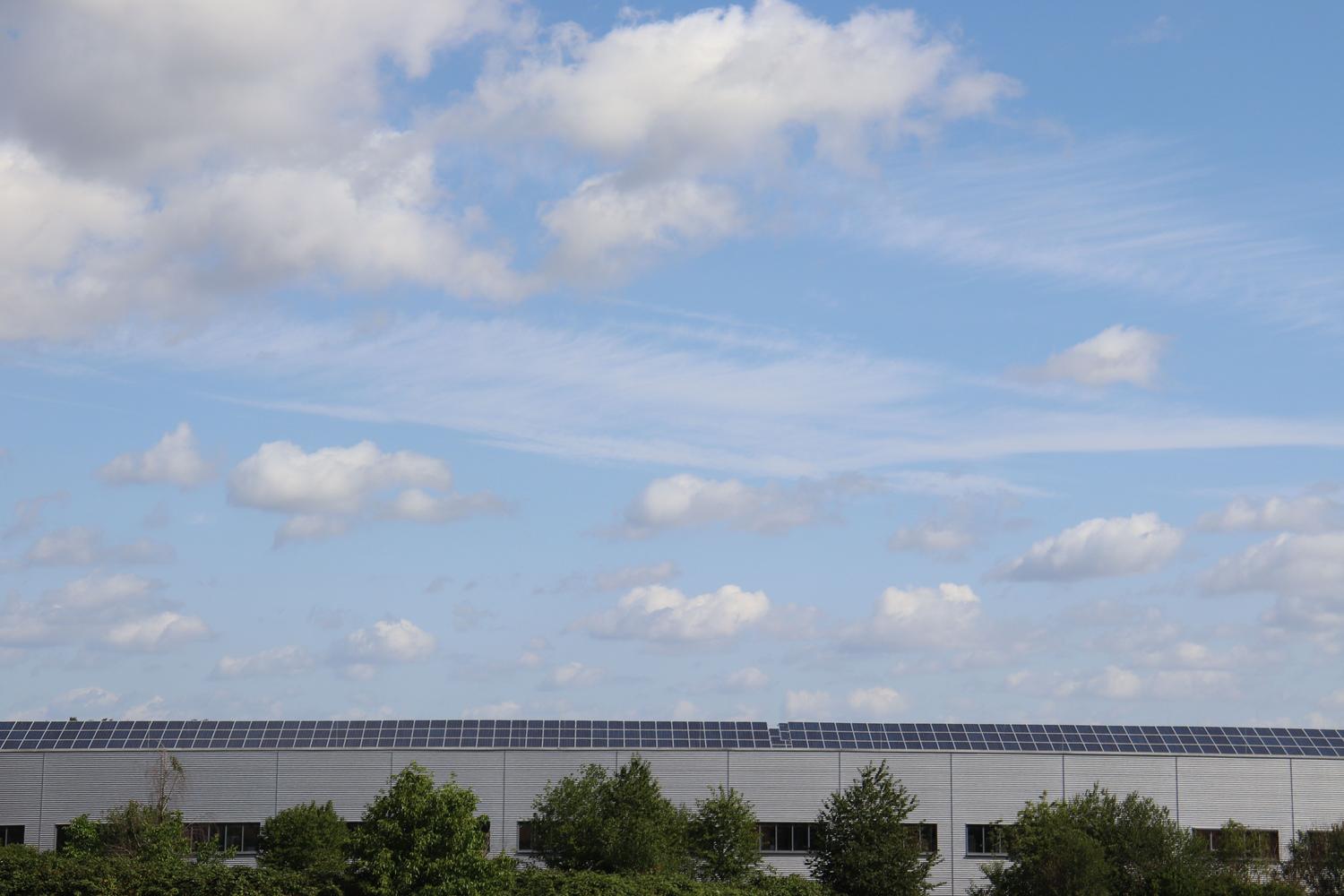 Instalación de paneles solares en la cumbrera del tejado de un almacén industrial bajo un cielo despejado.
