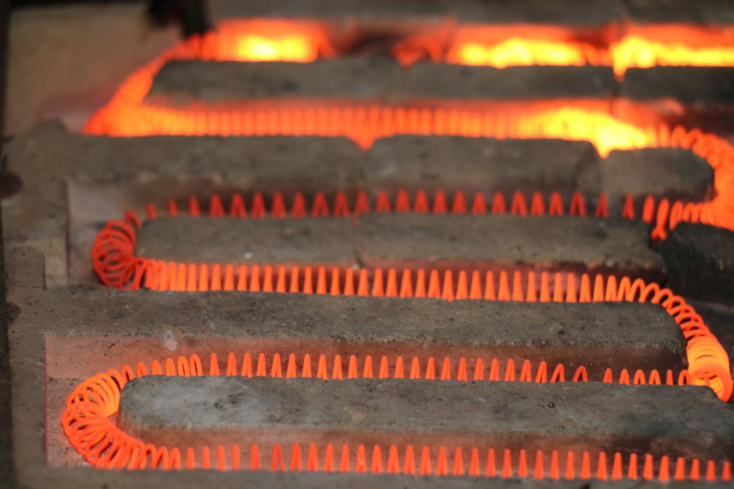 Primer plano de una resistencia eléctrica industrial incandescente generando calor intenso.