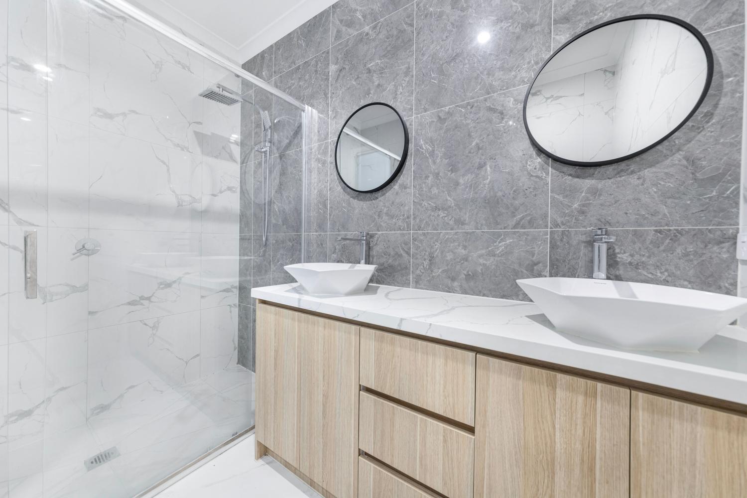 Diseño de baño elegante con azulejos de mármol blanco y lavabo doble, representando el resultado final de una reforma integral.