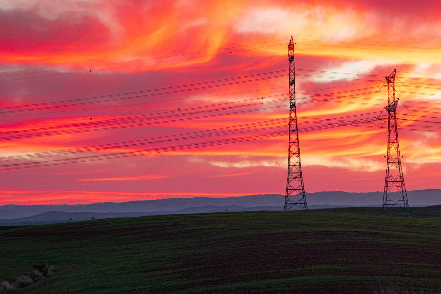 Torres de alta tensión silueteadas contra un colorido atardecer, representando la infraestructura de transporte eléctrico y los peajes.