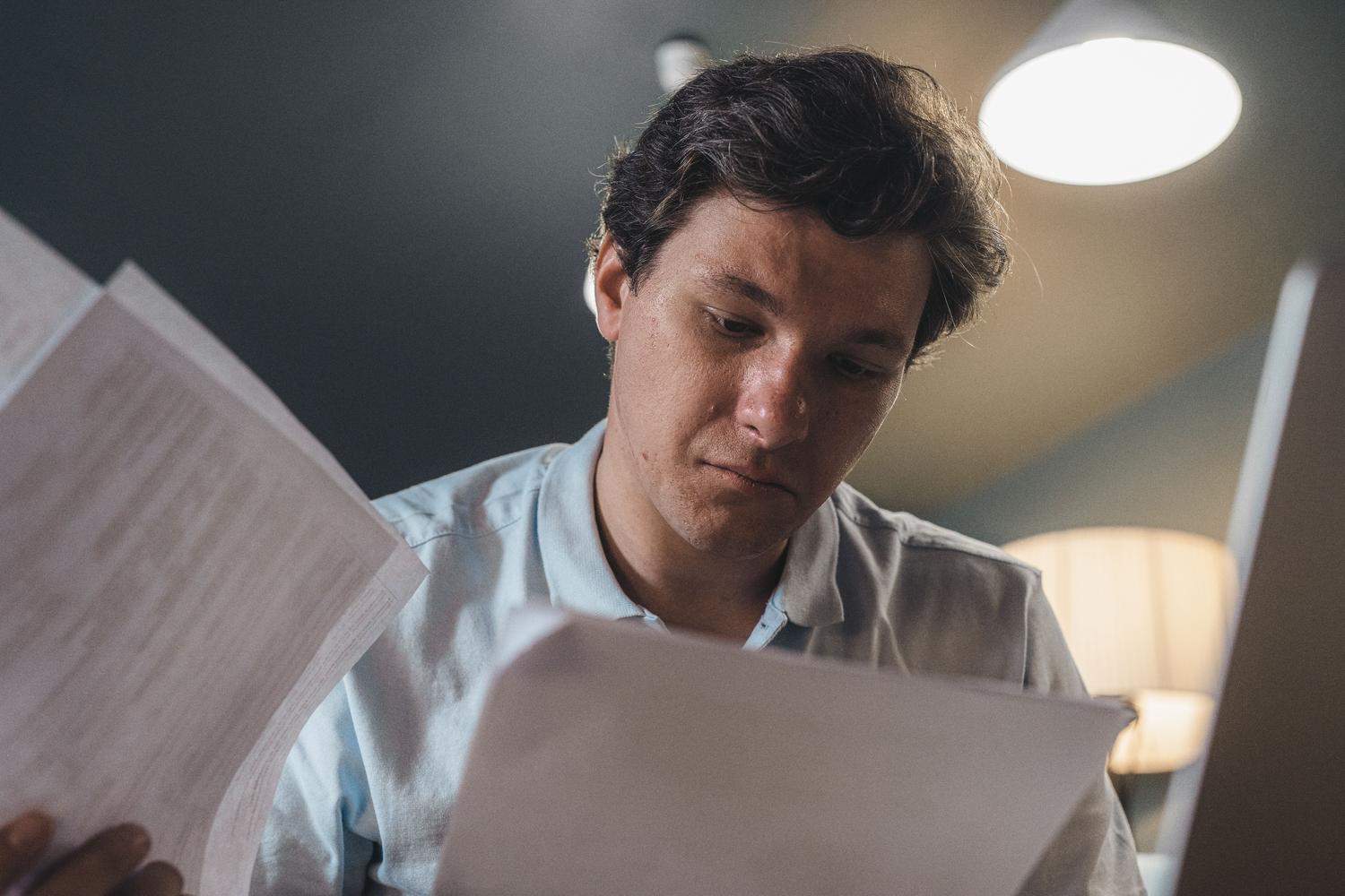 Hombre concentrado leyendo documentos impresos, ilustrando el análisis de los conceptos de peajes y cargos en una factura eléctrica.