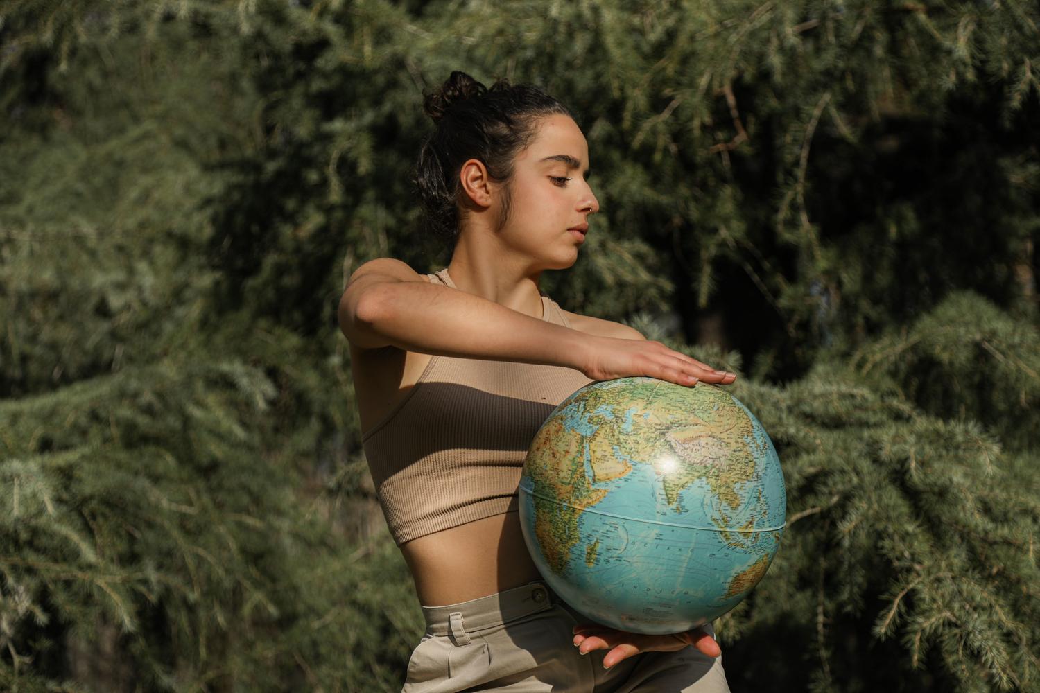 Mujer sosteniendo un globo terráqueo en un bosque, representando la conciencia global y los estándares internacionales de sostenibilidad.