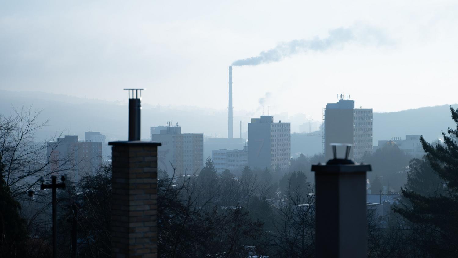 Paisaje urbano industrial con chimeneas y una atmósfera grisácea y brumosa, ilustrando la contaminación atmosférica general en entornos urbanos.