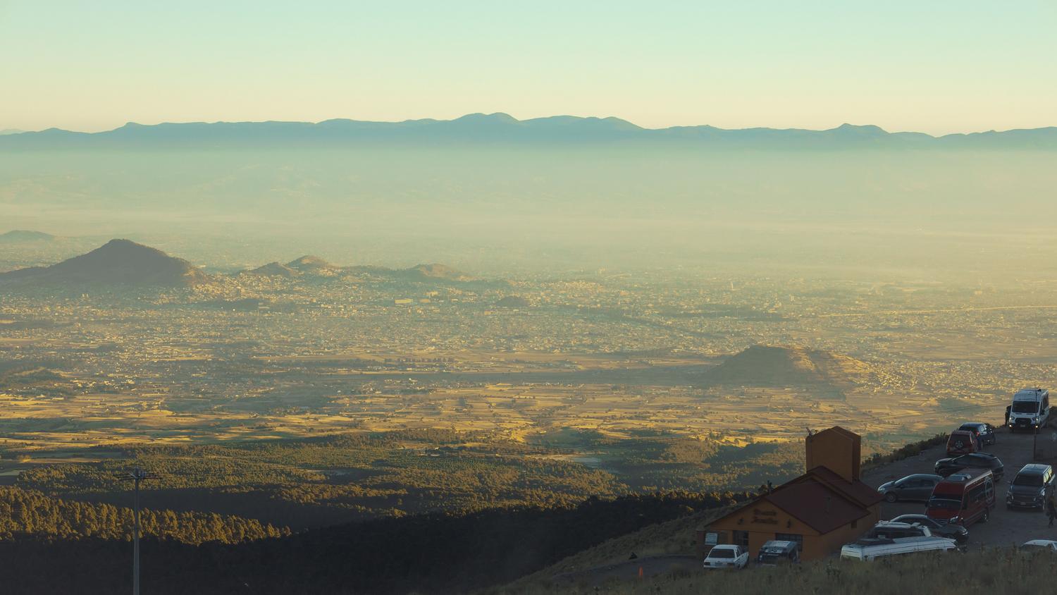 Vista aérea de una ciudad en un valle donde el smog queda atrapado, ejemplificando el fenómeno de la inversión térmica y la acumulación de contaminantes.