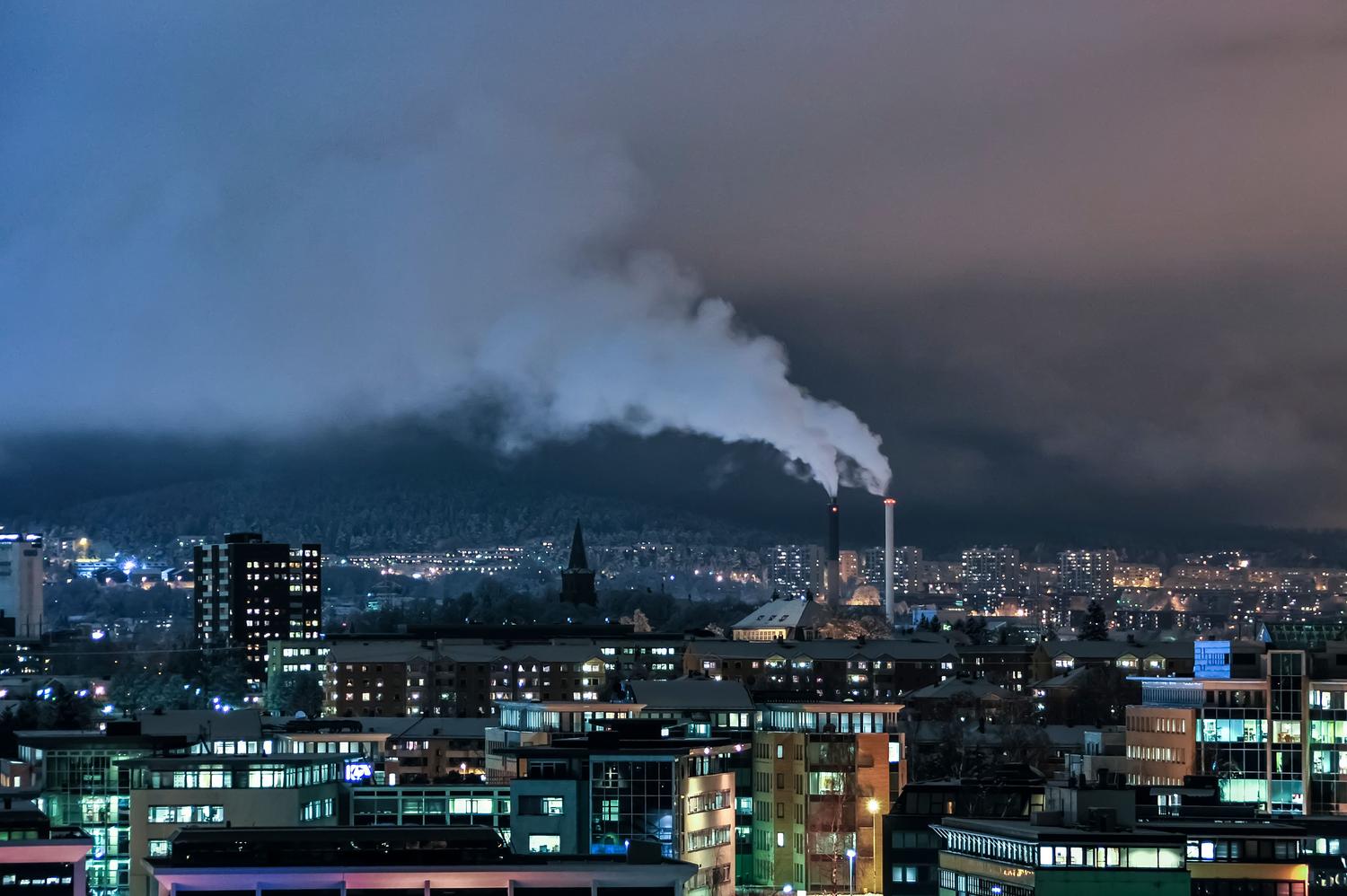 Vista nocturna de una zona industrial con emisiones de humo, aportando una perspectiva diferente sobre la actividad contaminante constante en las ciudades.