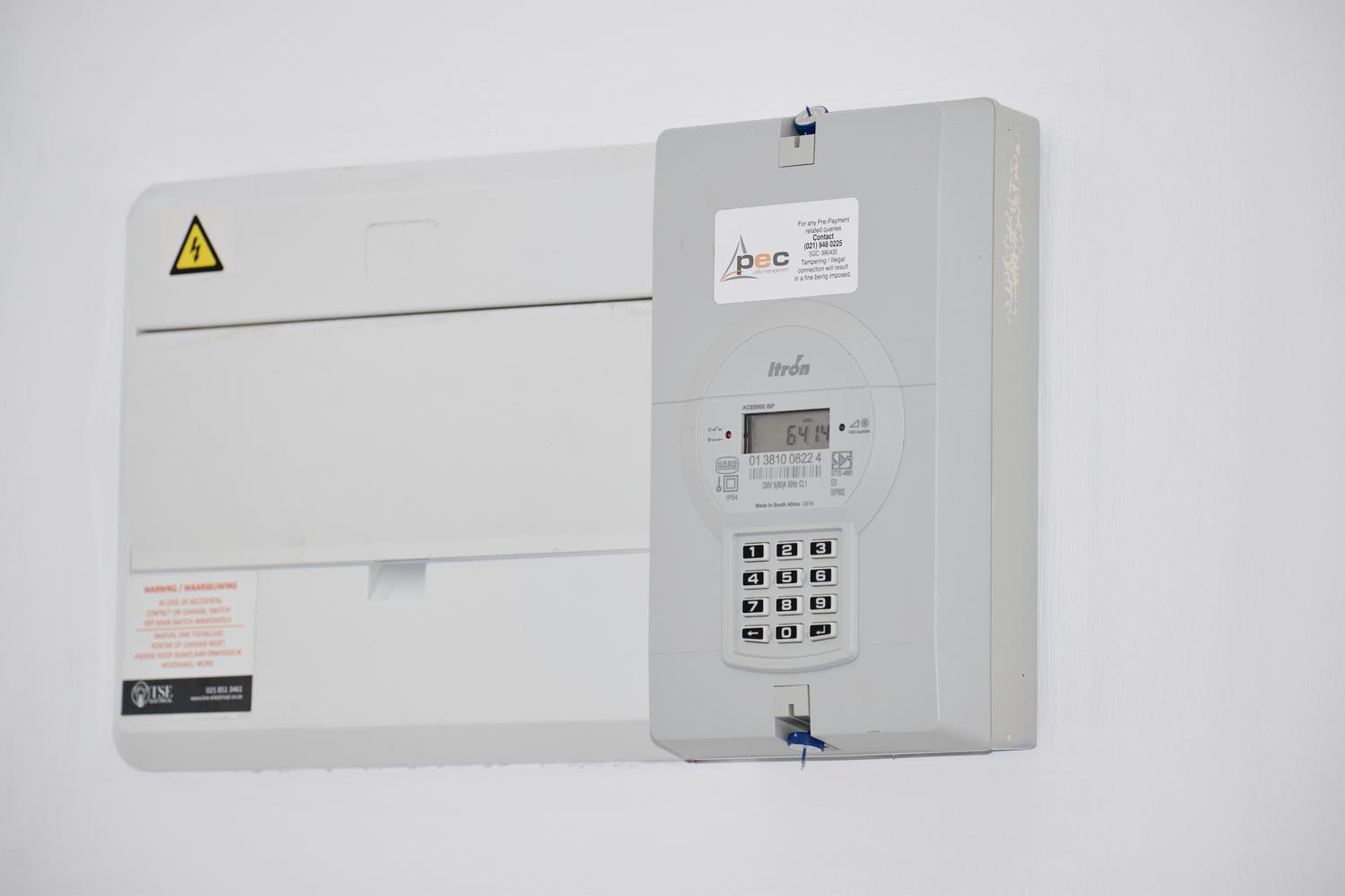 Detalle de un medidor de luz digital y un cuadro de distribución eléctrica en una pared blanca.