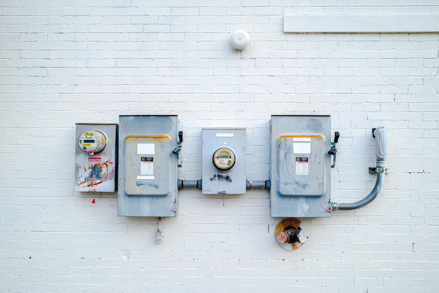 Instalación de múltiples cajas eléctricas y medidores de luz en una pared de ladrillo blanco.