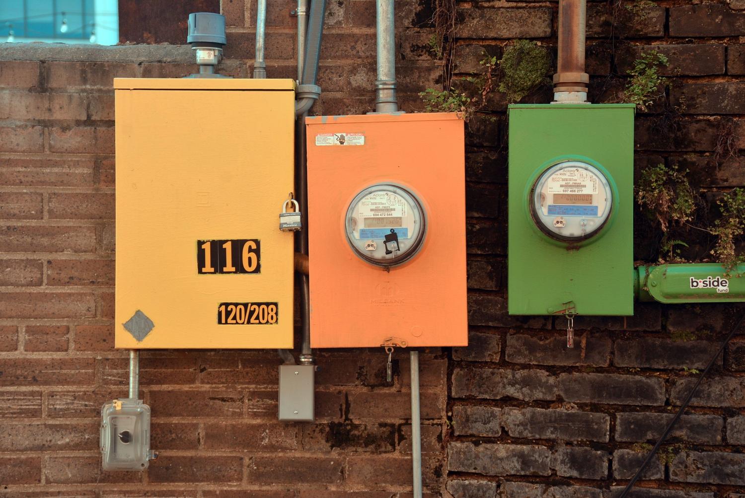 Tres medidores de servicios públicos de diferentes colores instalados en una pared de ladrillo.