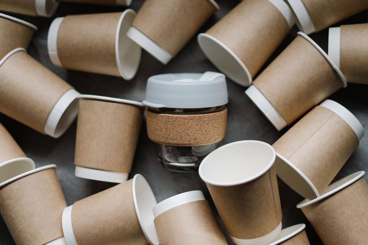 Comparativa entre una taza reutilizable y vasos de papel desechables, ilustrando la reducción de residuos y el consumo consciente.