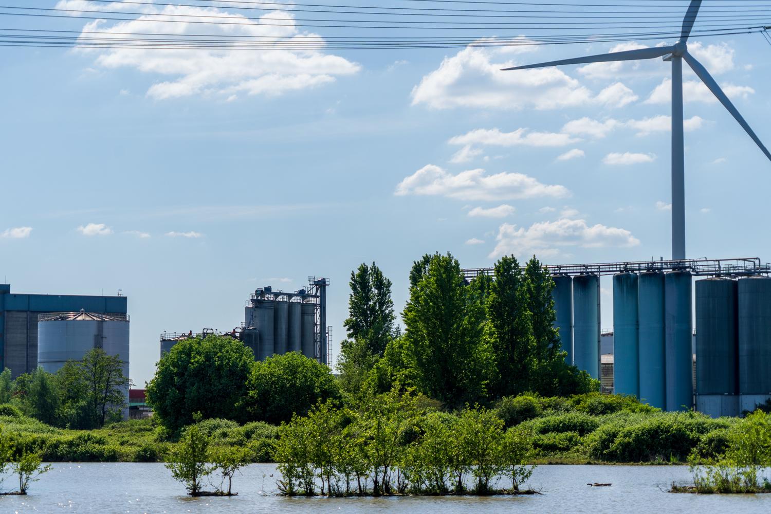 Paisaje industrial sostenible con un aerogenerador y naturaleza circundante, simbolizando la armonía entre industria y medio ambiente.