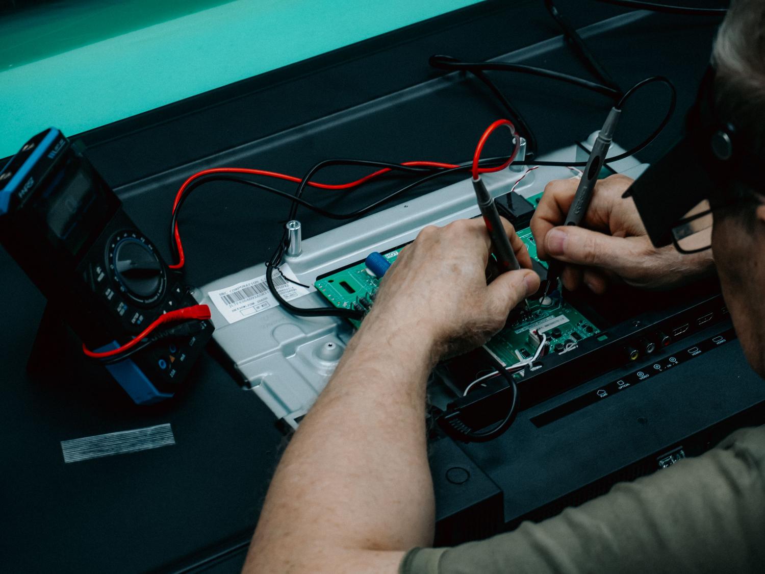 Técnico especializado utilizando un multímetro para analizar una placa de circuito electrónico, esencial para la seguridad en talleres eléctricos.