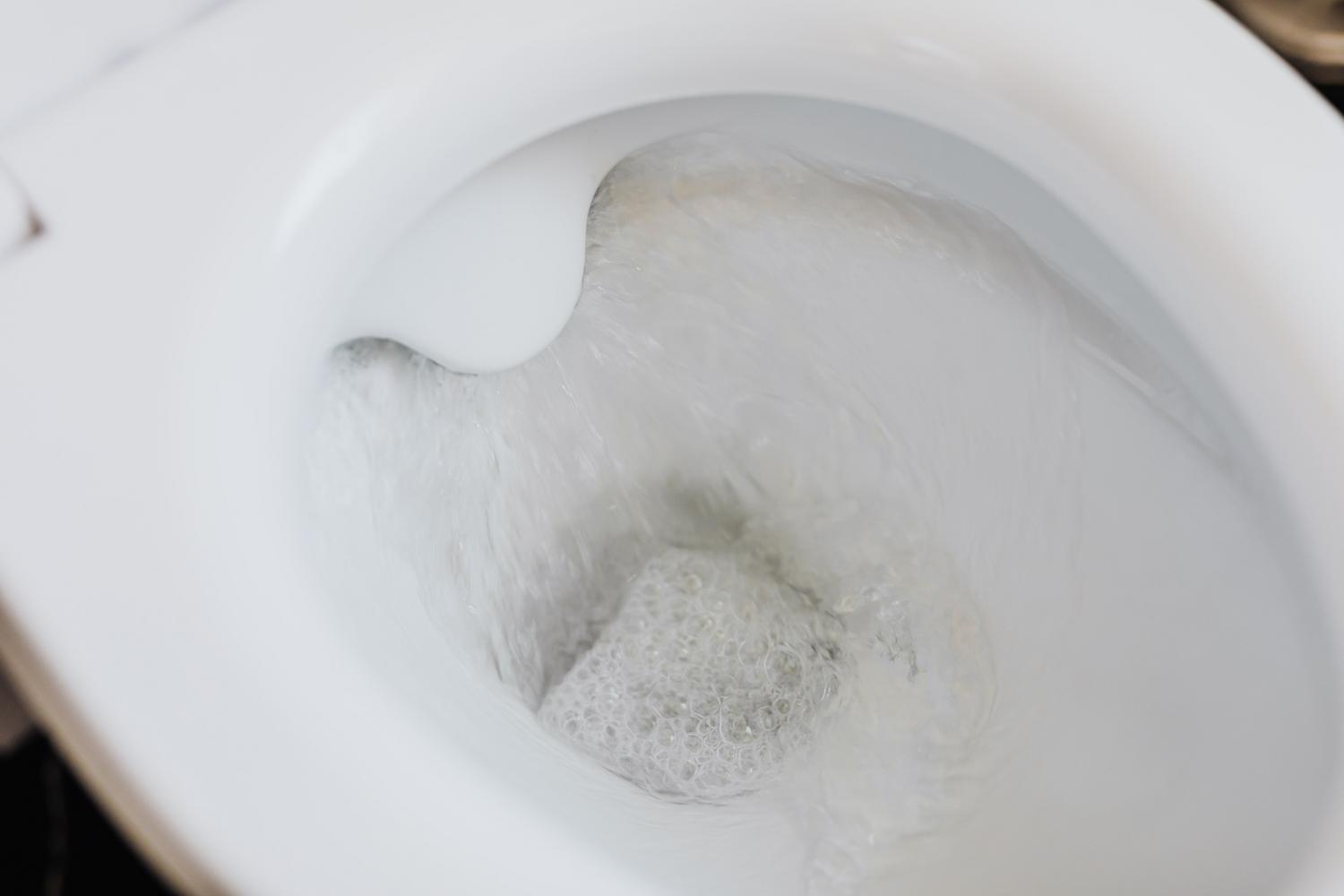 Imagen de un inodoro blanco impecable con agua jabonosa al tirar de la cadena.