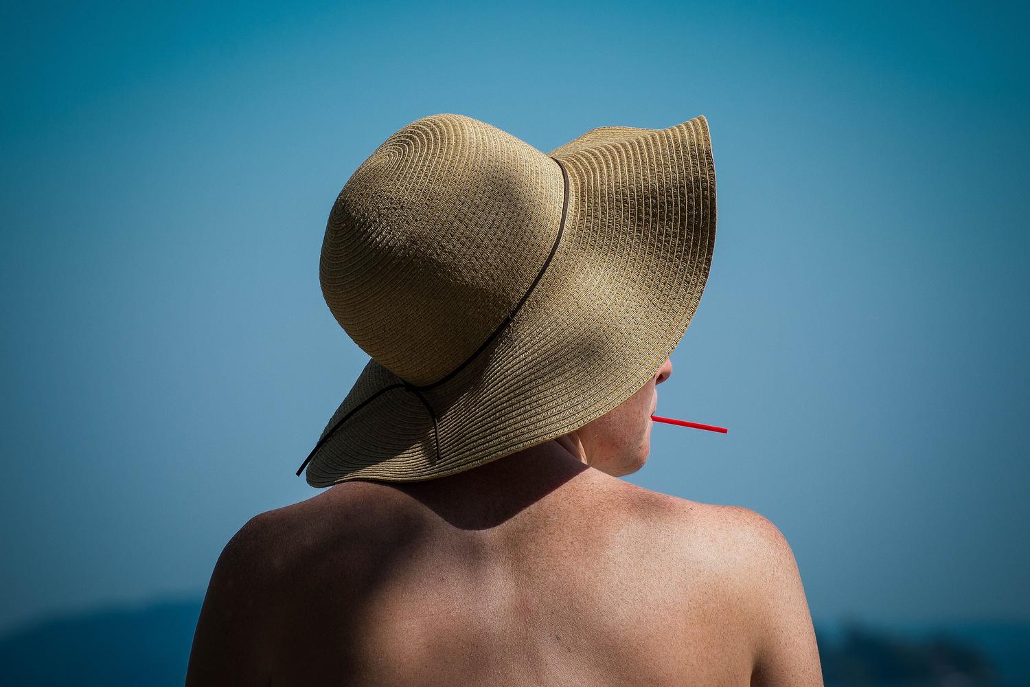 Mujer utilizando un sombrero de ala ancha en la playa para evitar la exposición directa al sol.