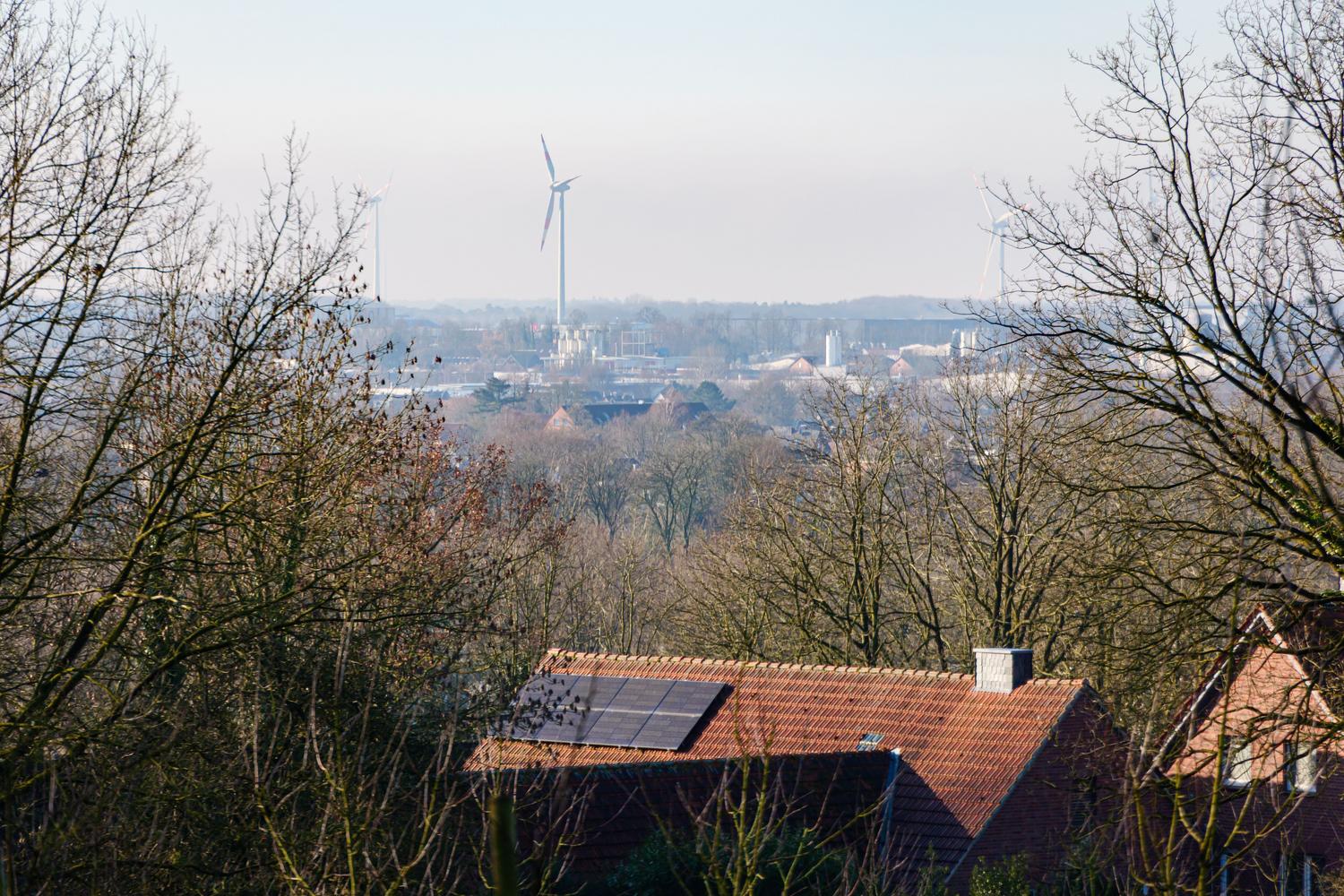Vista urbana con paneles solares en tejados y aerogeneradores al fondo, ilustrando la diversificación de fuentes energéticas locales.