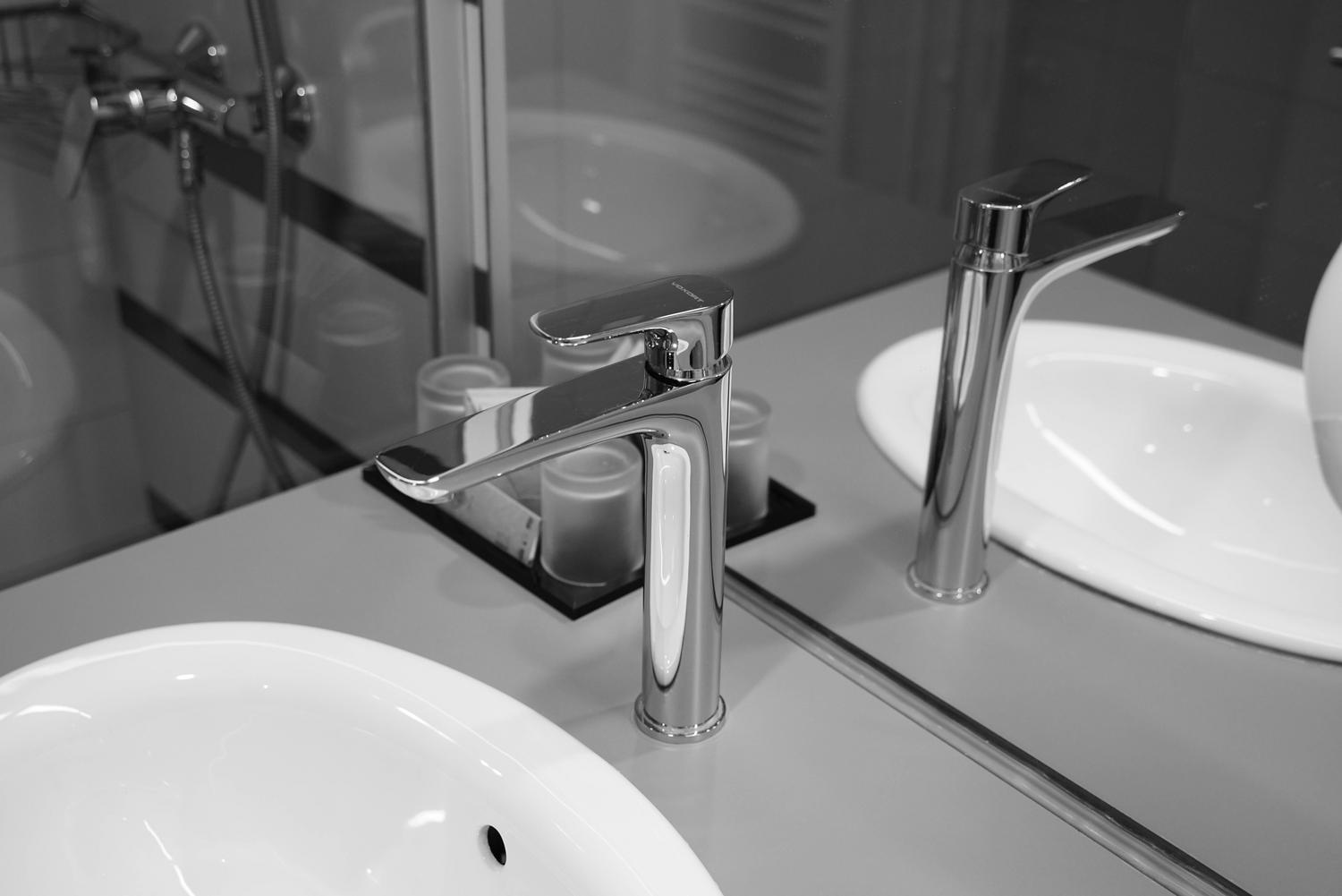 Grifo de acero inoxidable de diseño minimalista en un baño monocromático, enfatizando la durabilidad y la sobriedad.