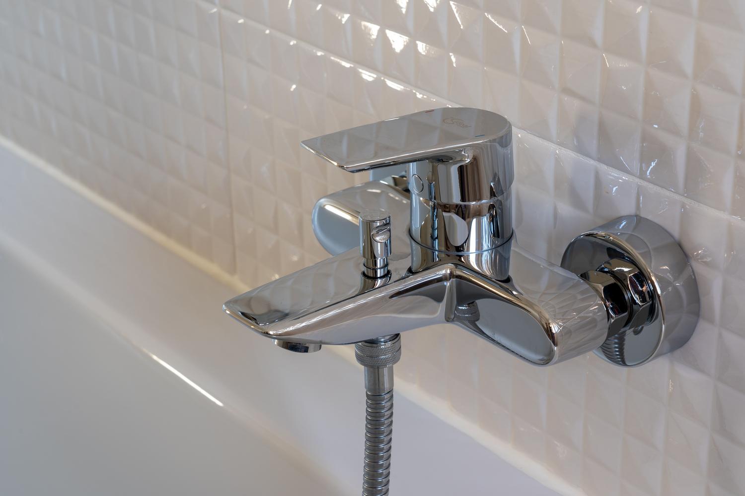 Grifo de baño moderno cromado con azulejos geométricos blancos, destacando un diseño minimalista y limpio.
