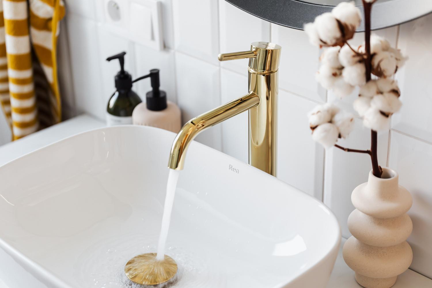 Grifería de lujo en color oro con agua corriendo en un lavabo blanco, transmitiendo elegancia y exclusividad.