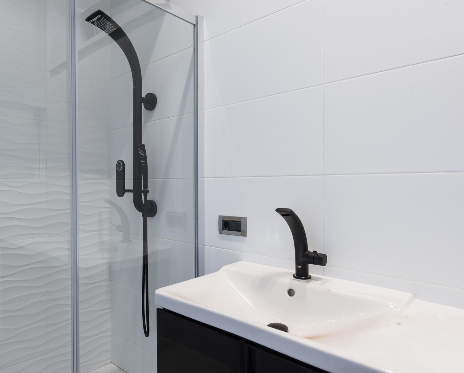 Baño minimalista con grifo y sistema de ducha en negro mate, ideal para ambientes contemporáneos y sofisticados.