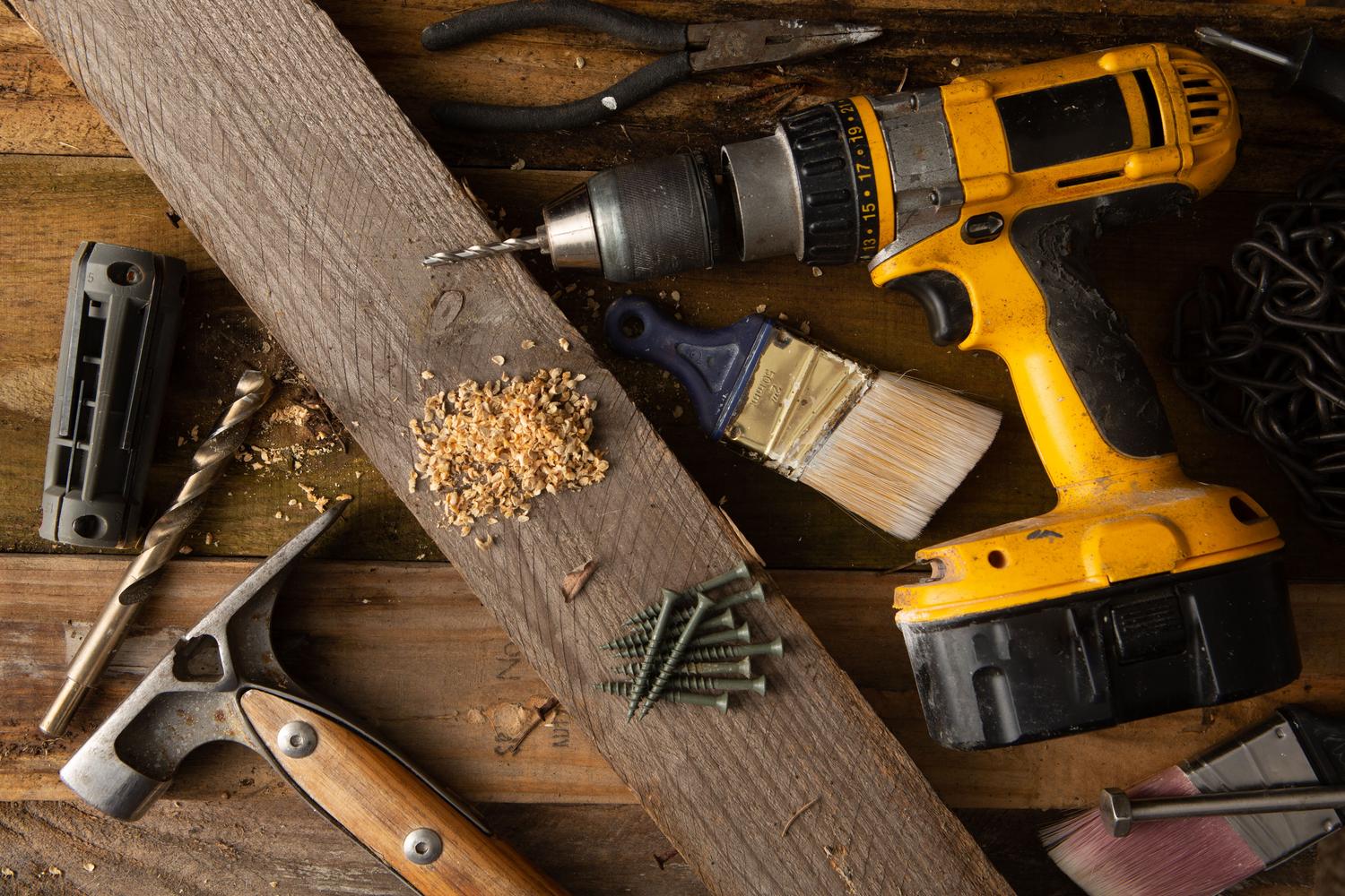 Taladro inalámbrico y herramientas manuales sobre un banco de trabajo rústico con virutas de madera