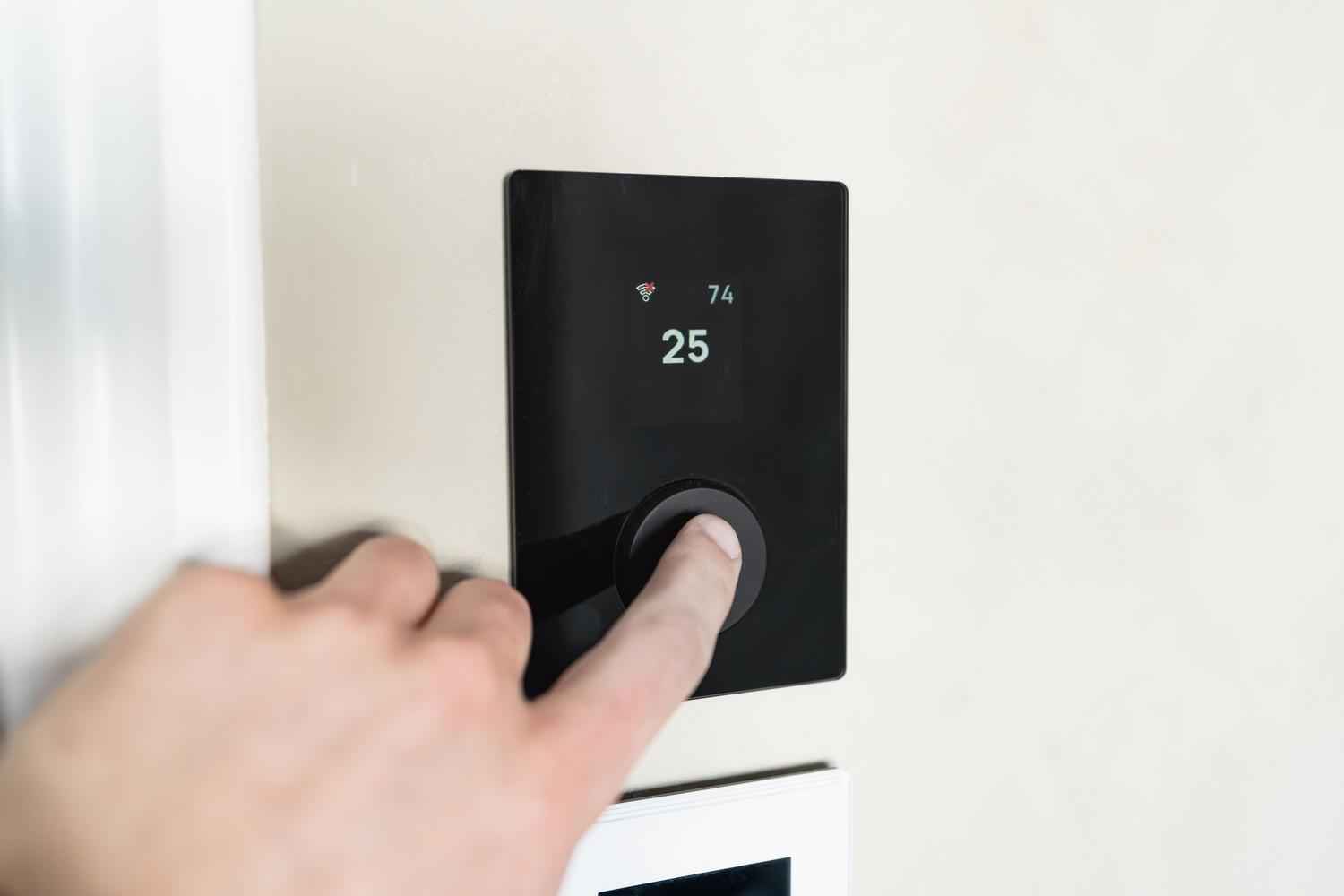 Primer plano de una mano ajustando un termostato inteligente digital para optimizar la climatización en la oficina.