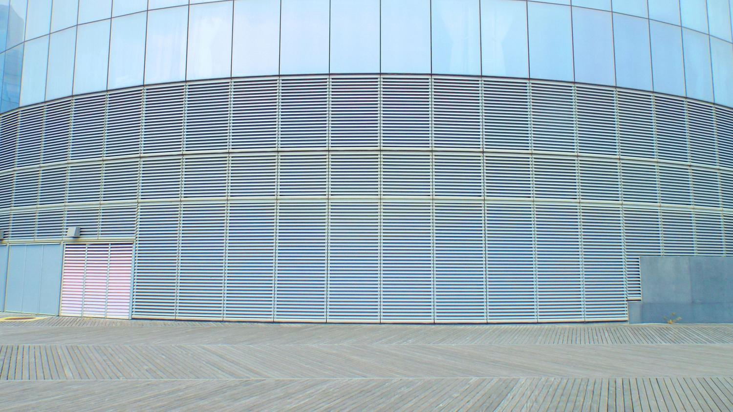 Fachada de edificio moderno con sistemas de sombreado exterior y lamas metálicas para optimizar el control solar y la eficiencia energética.