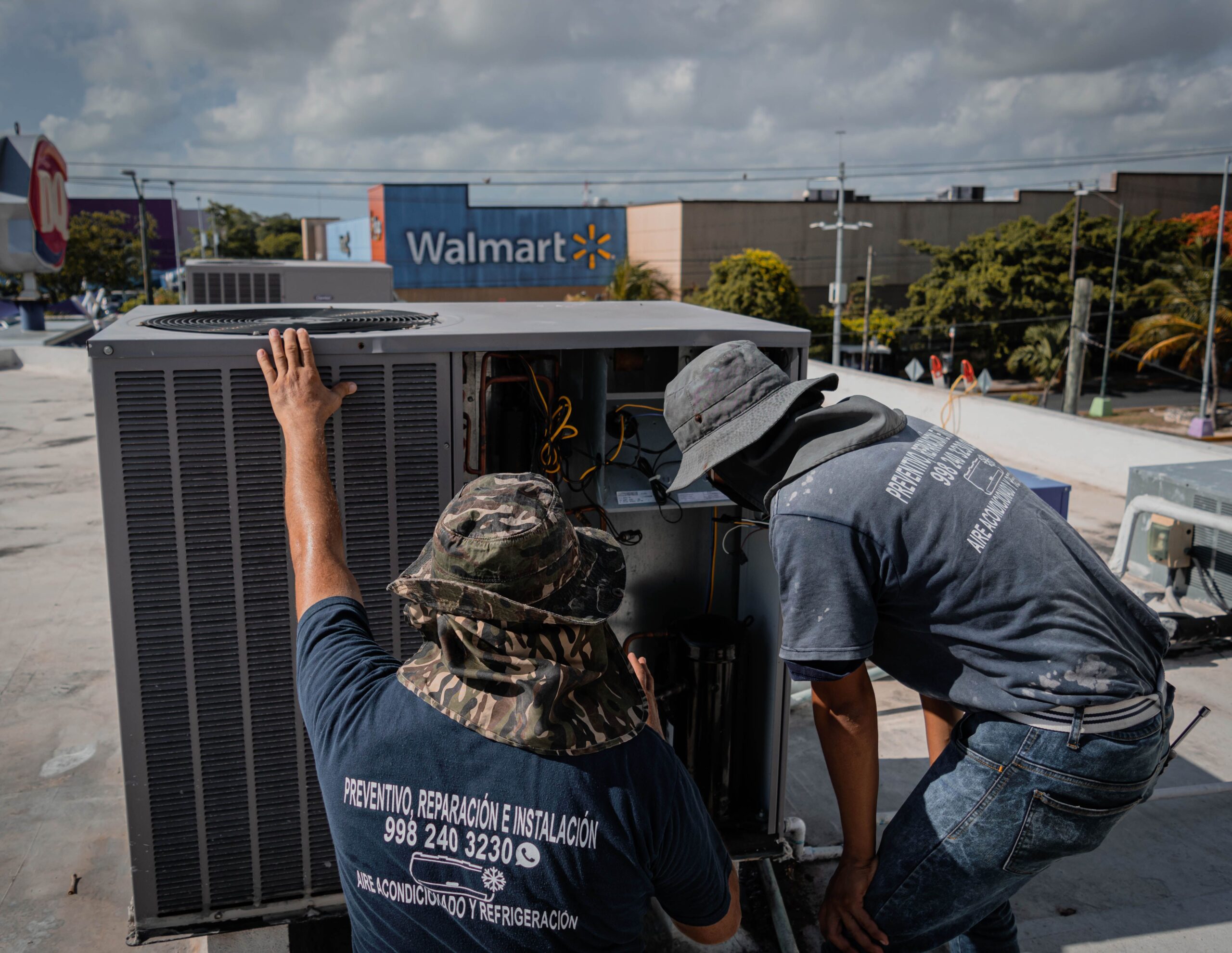 Técnicos de HVAC realizando labores de mantenimiento preventivo y reparación en una unidad de aire acondicionado en una azotea.