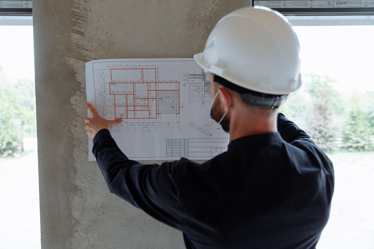 Ingeniero con casco de seguridad revisando detalladamente planos arquitectónicos en una obra, representando al técnico certificador.