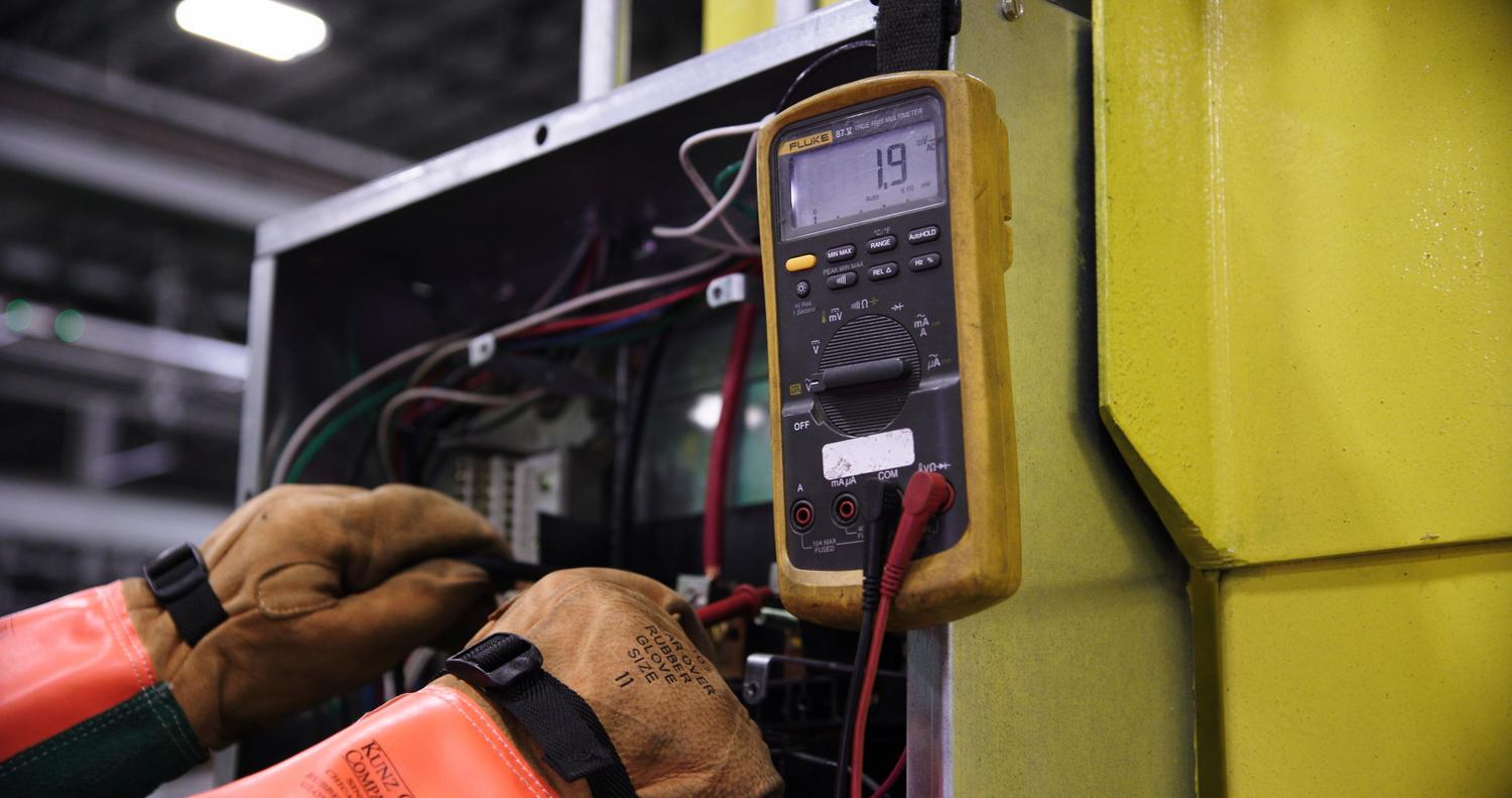 Electricista profesional utilizando un multímetro para verificar la seguridad y el correcto funcionamiento de un panel eléctrico.