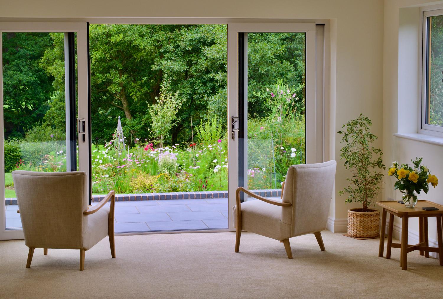 Interior acogedor con sillones y vista al jardín a través de grandes puertas correderas de cristal.