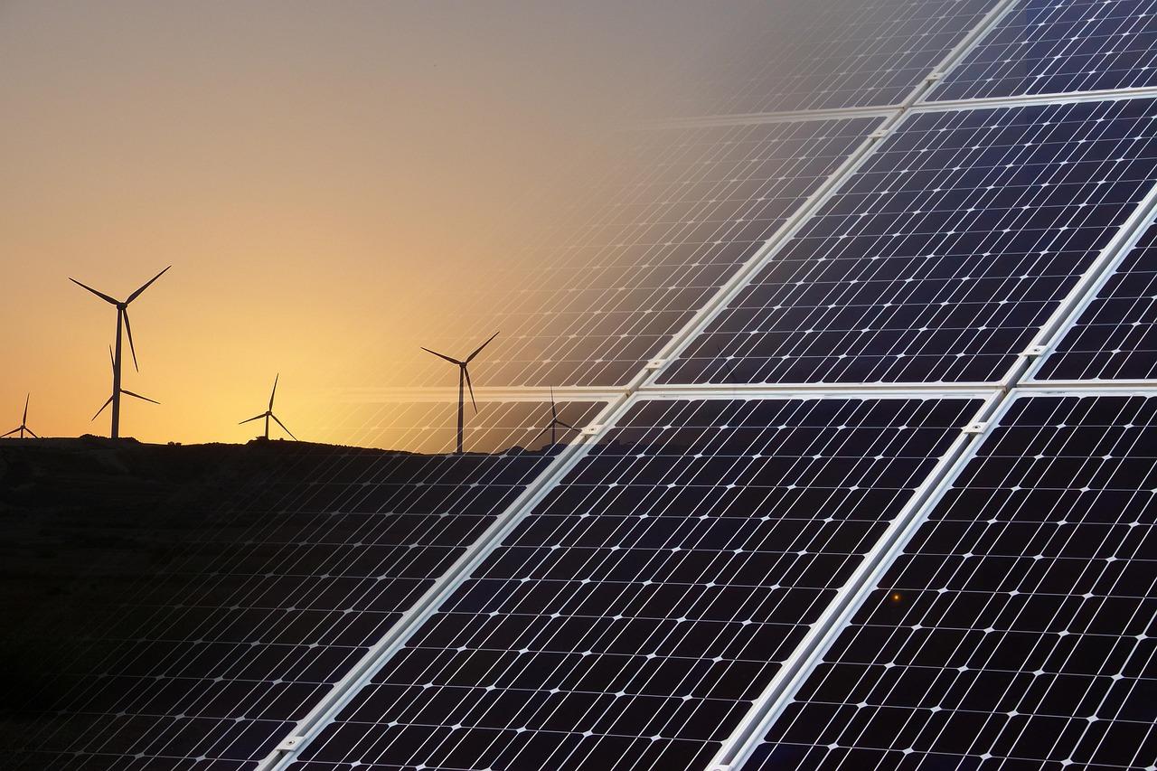 Combinación de paneles solares y turbinas eólicas al atardecer, representando la transición hacia las energías renovables.