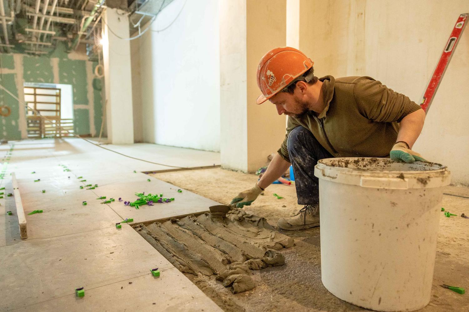 Obrero de la construcción colocando azulejos en el suelo durante una obra de remodelación de local comercial