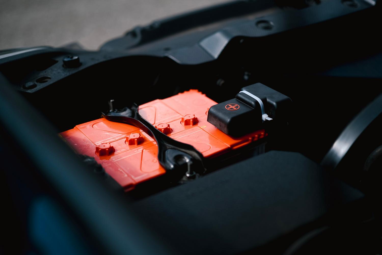 Primer plano de una batería de coche instalada en el compartimento del motor, mostrando sus bornes y estructura.