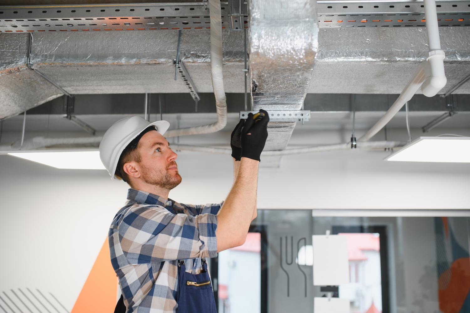 Obrero de la construcción instalando conductos de ventilación y climatización en la estructura de un edificio