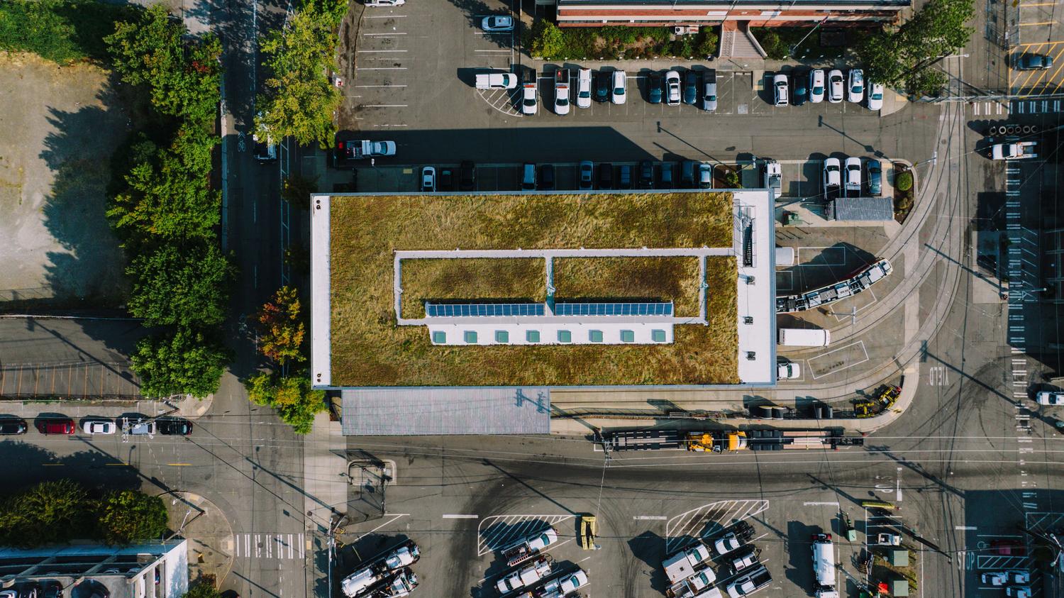 Vista aérea de una azotea biosolar con paneles fotovoltaicos integrados sobre un techo verde con vegetación urbana en un entorno citadino.