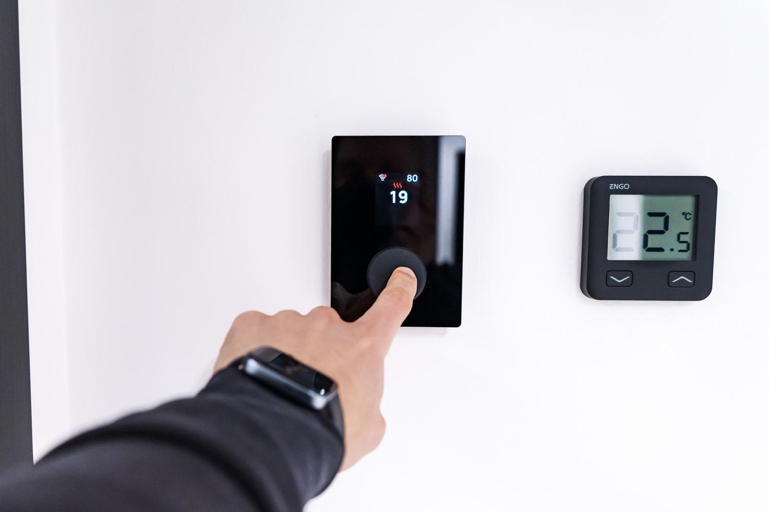 Primer plano de una mano ajustando un termostato digital inteligente en un interior moderno, ilustrando la digitalización y el IoT en la climatización.