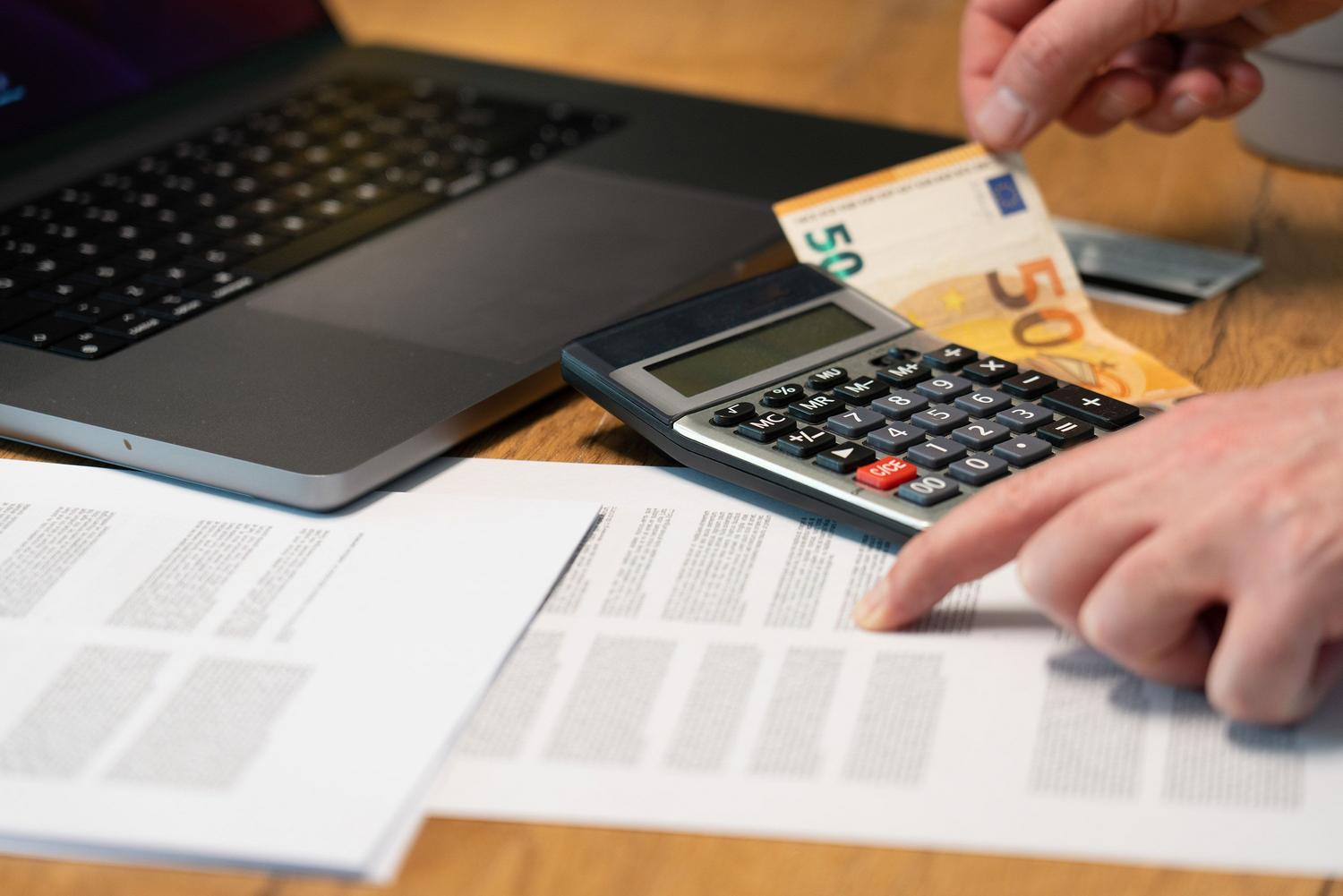 Primer plano de manos utilizando una calculadora y billetes de euro junto a documentos, ideal para explicar el cálculo del término fijo.
