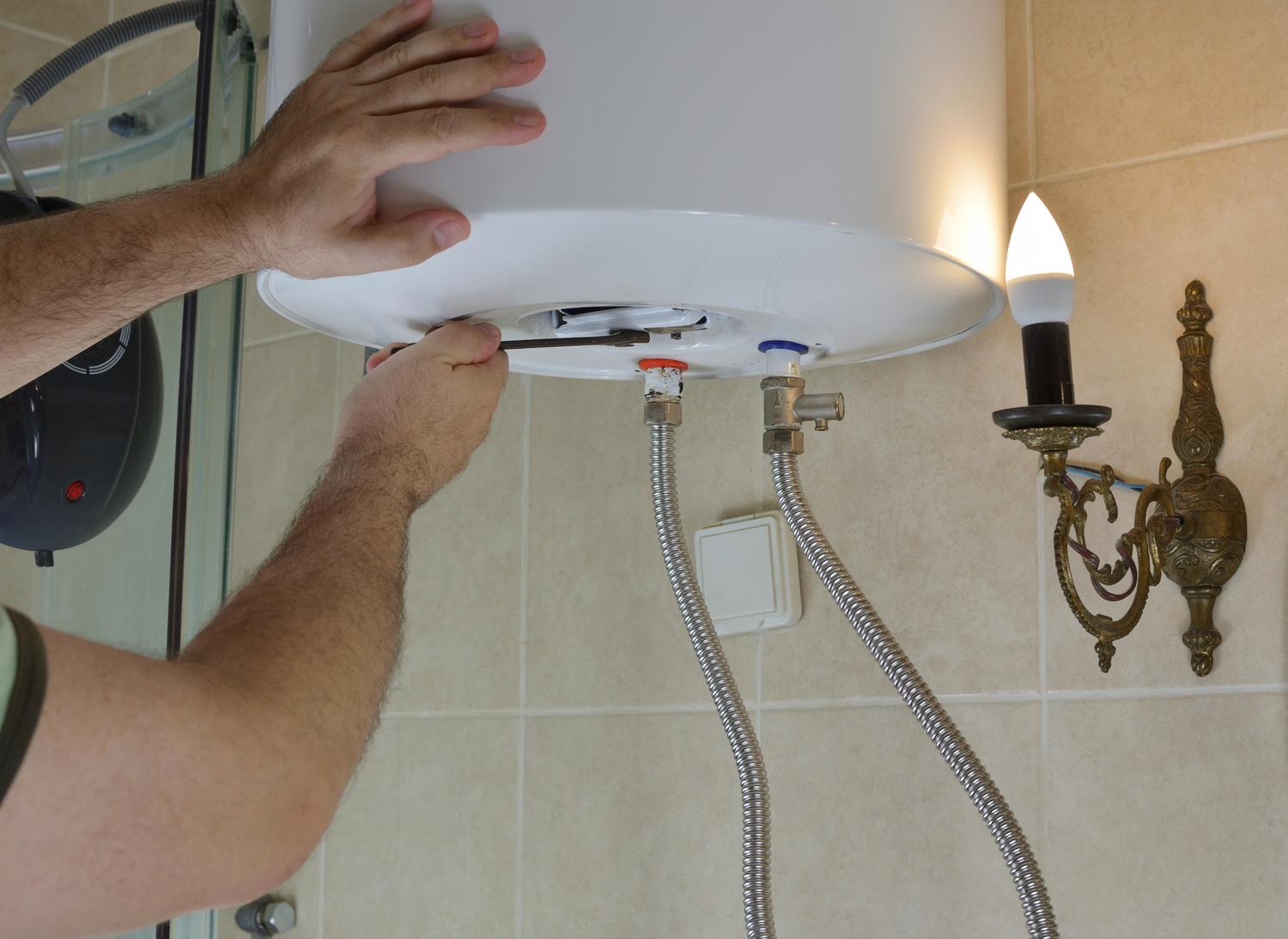 Manos de un técnico utilizando una llave inglesa para realizar el mantenimiento preventivo de un termo eléctrico en un baño.