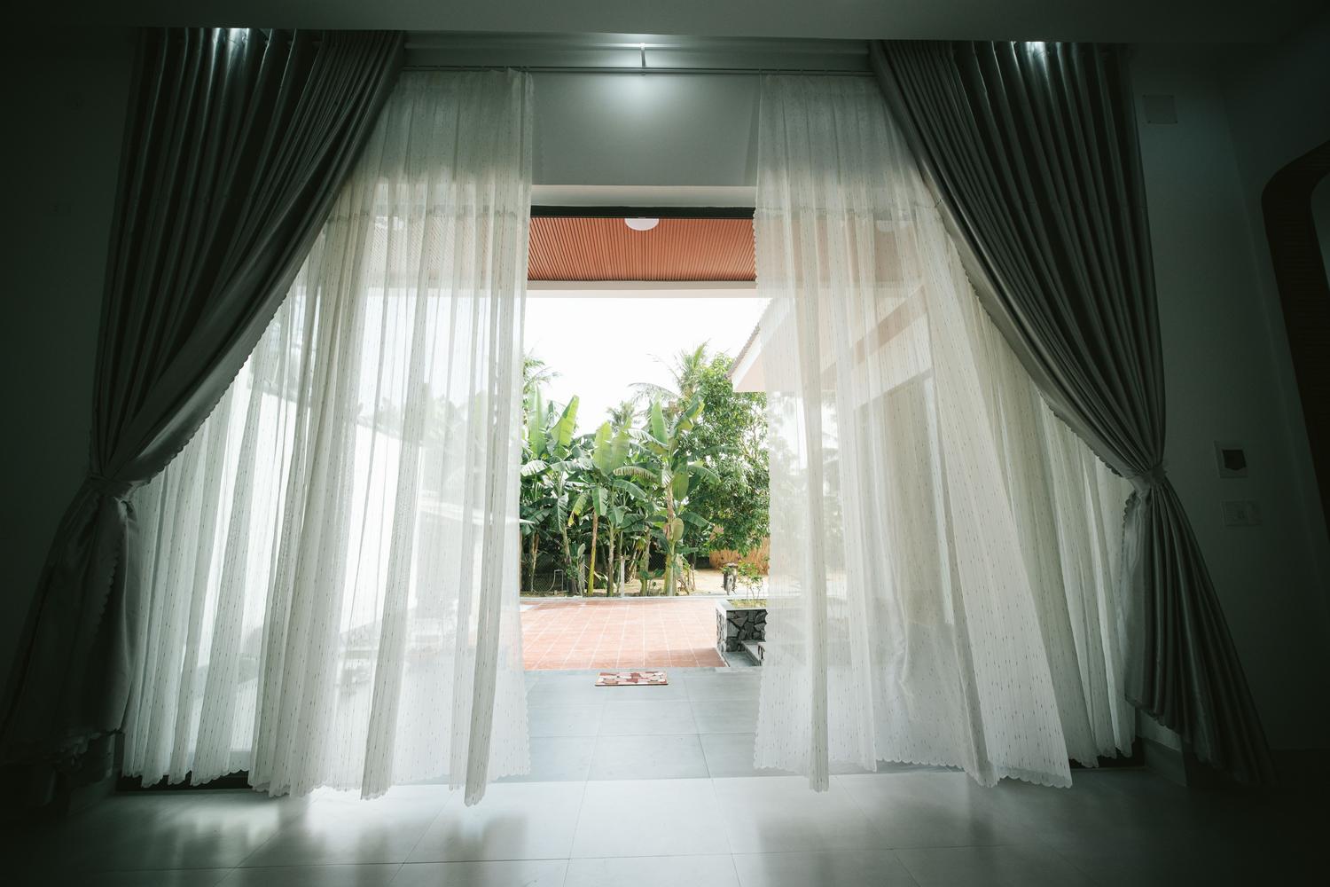 Ventana abierta con cortinas blancas ondeando suavemente, sugiriendo una corriente de aire natural.